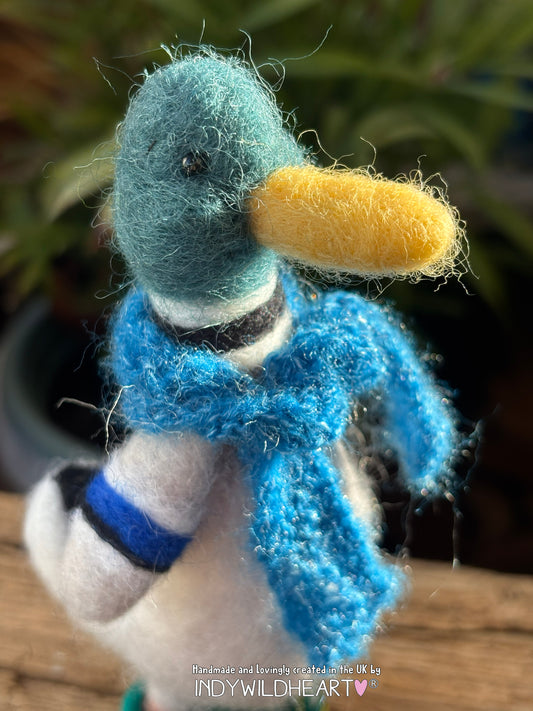 Handmade duck figurine with a blue scarf and yellow beak on a blurred natural background