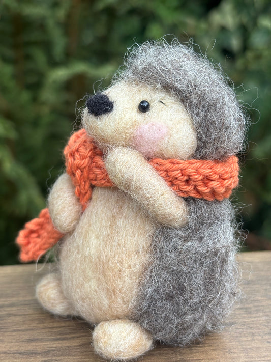 Hedgehog felt decoration with an orange scarf against a blurred green background