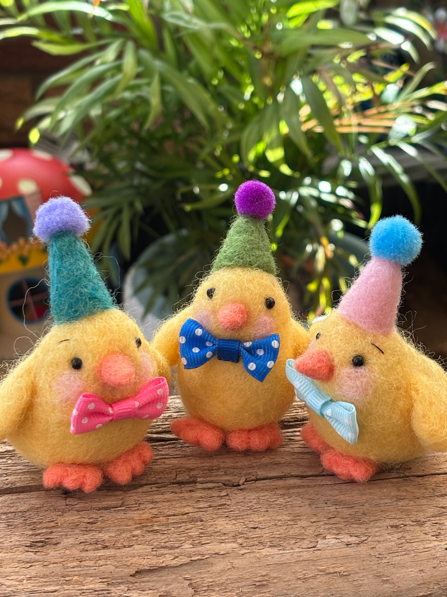 Three colorful felt chicks with party hats on a wooden surface.