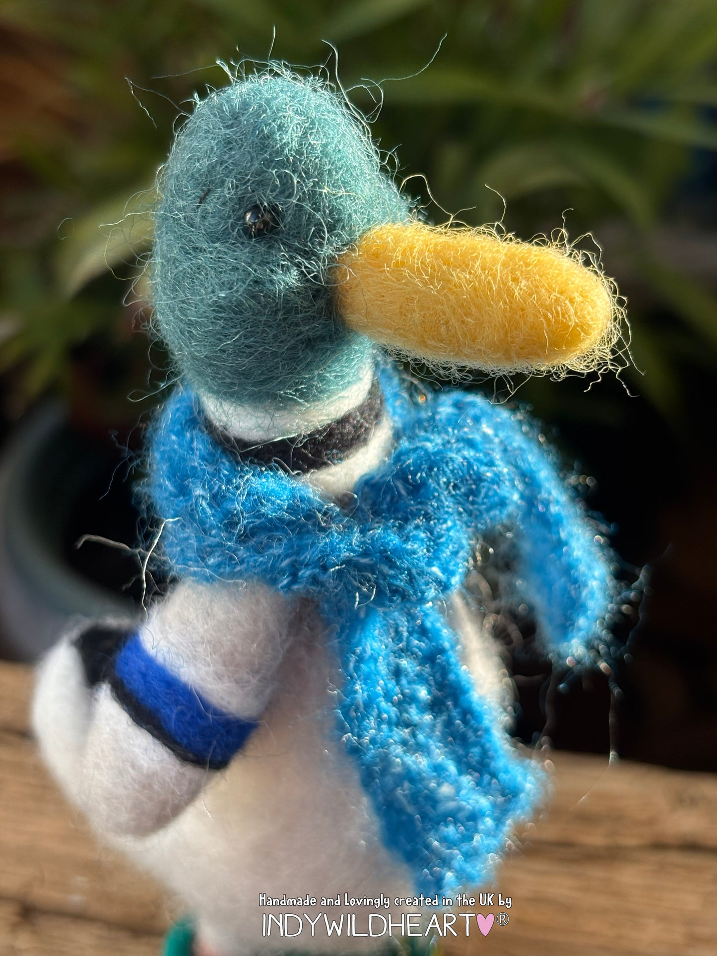 Handmade duck figurine with a blue scarf and yellow beak on a blurred natural background