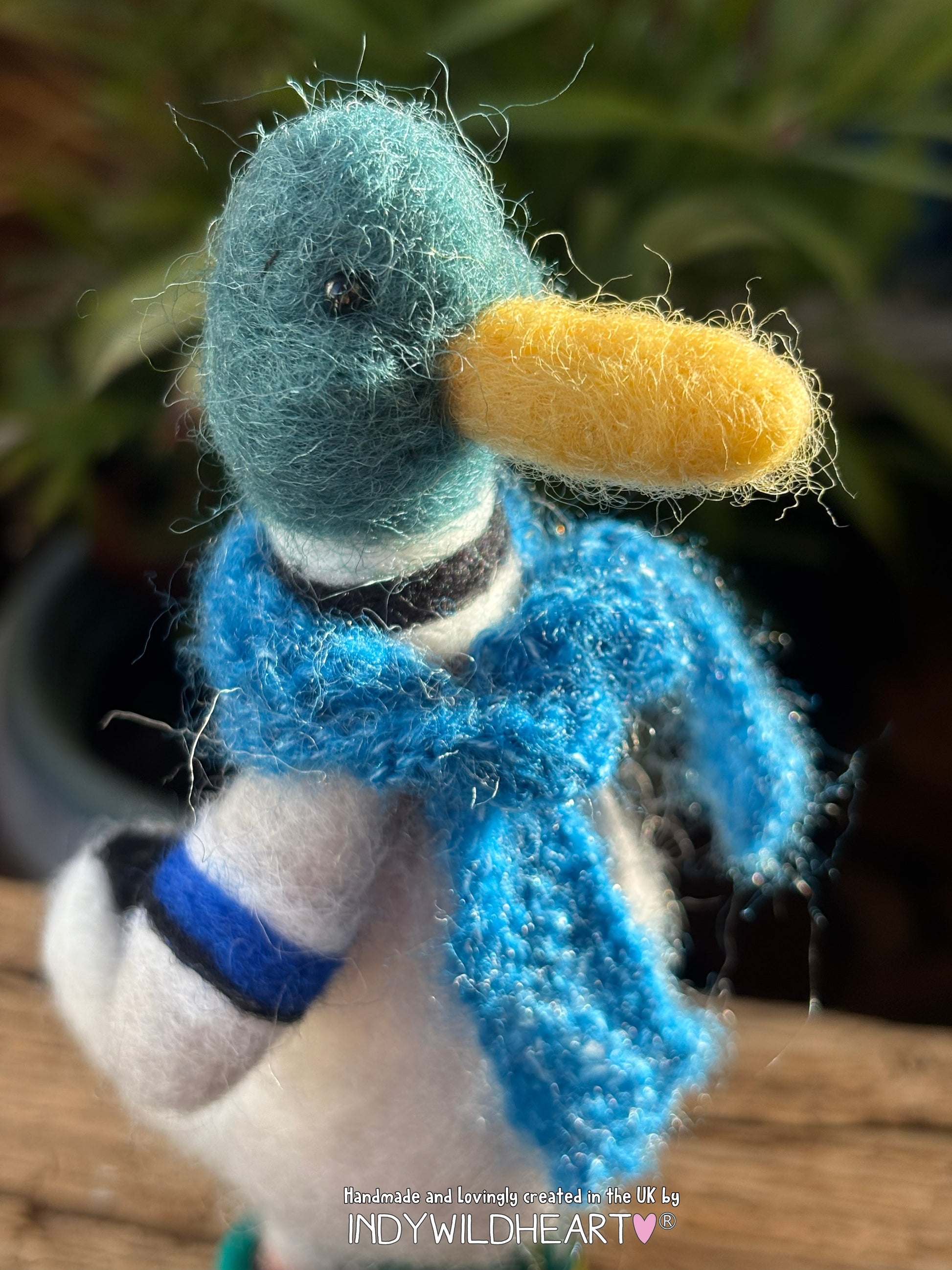 Handmade duck figurine with a blue scarf and yellow beak on a blurred natural background