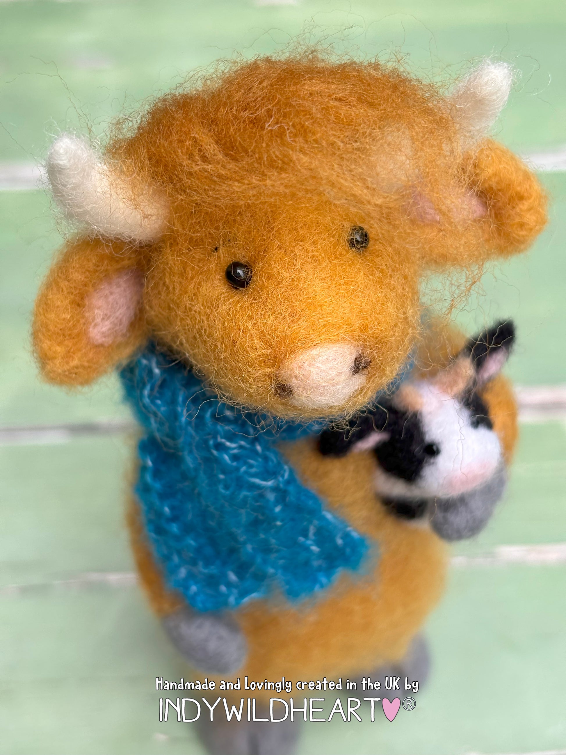 Handmade brown felted highland cow with a blue scarf and small black and white teddy. 
