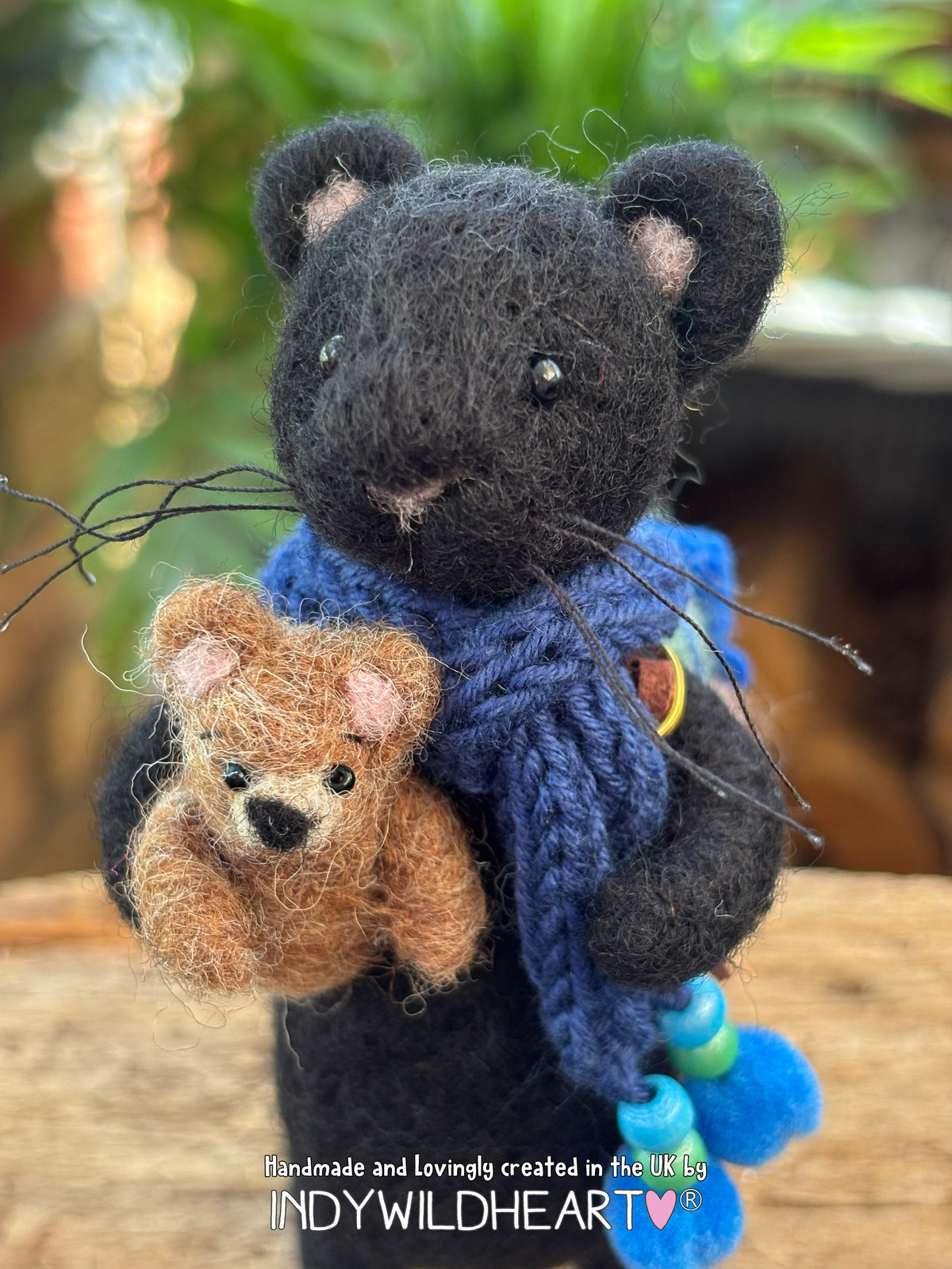 Needle Felted Black Panther character with navy blue scarf and holding a miniature needle felted teddy