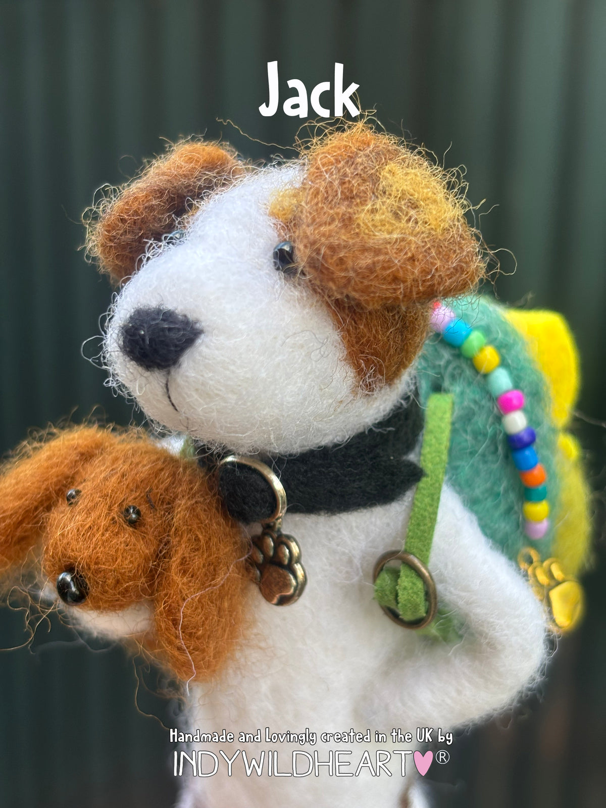 A handmade needle felted wool dog collectible named Jack, featuring a white and brown body, a black collar with gold paw charm, and a green backpack with colorful beads. The background is a dark green textured wall.