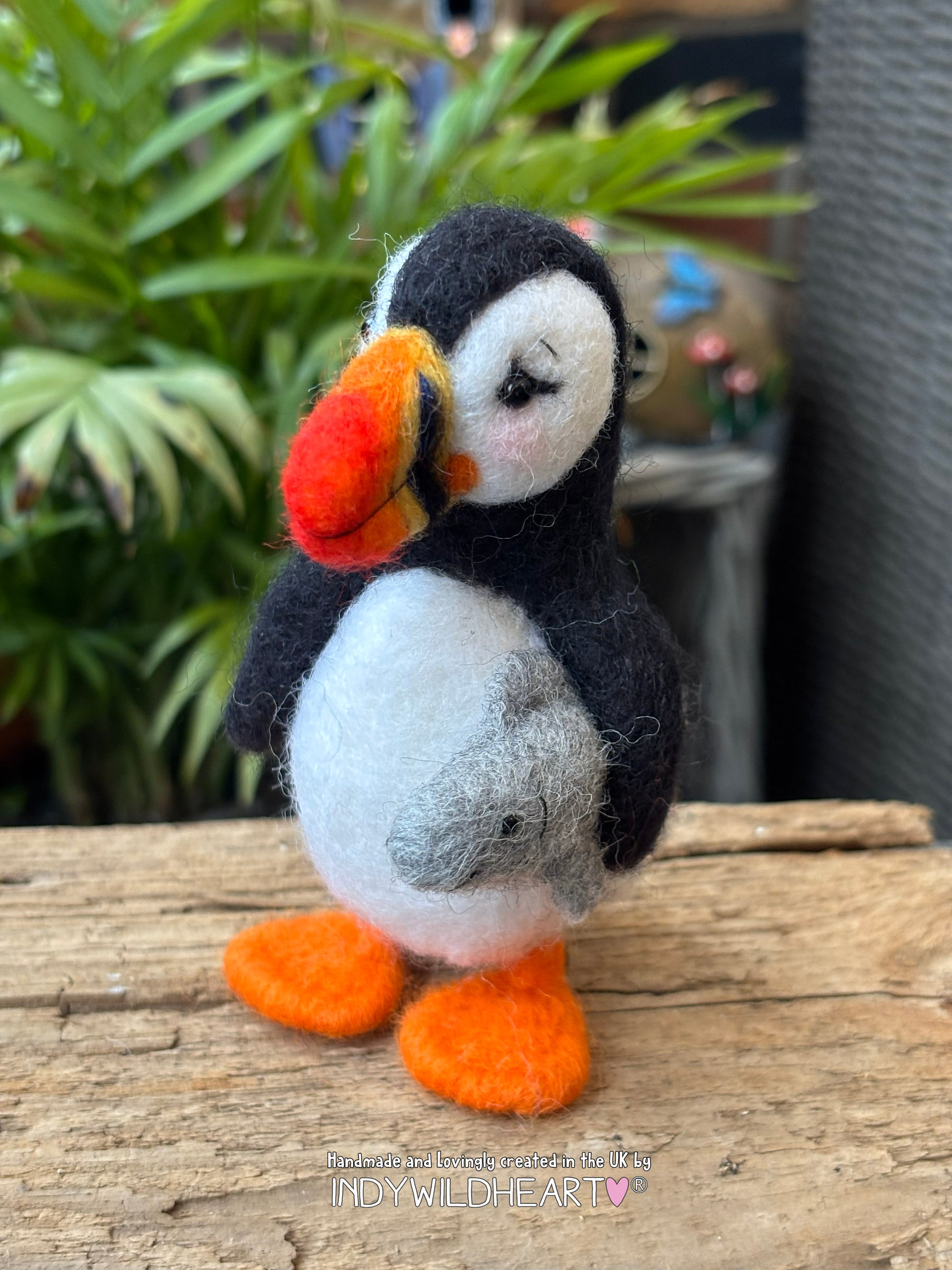 needle felted puffin toy on a wooden surface with plants in the background