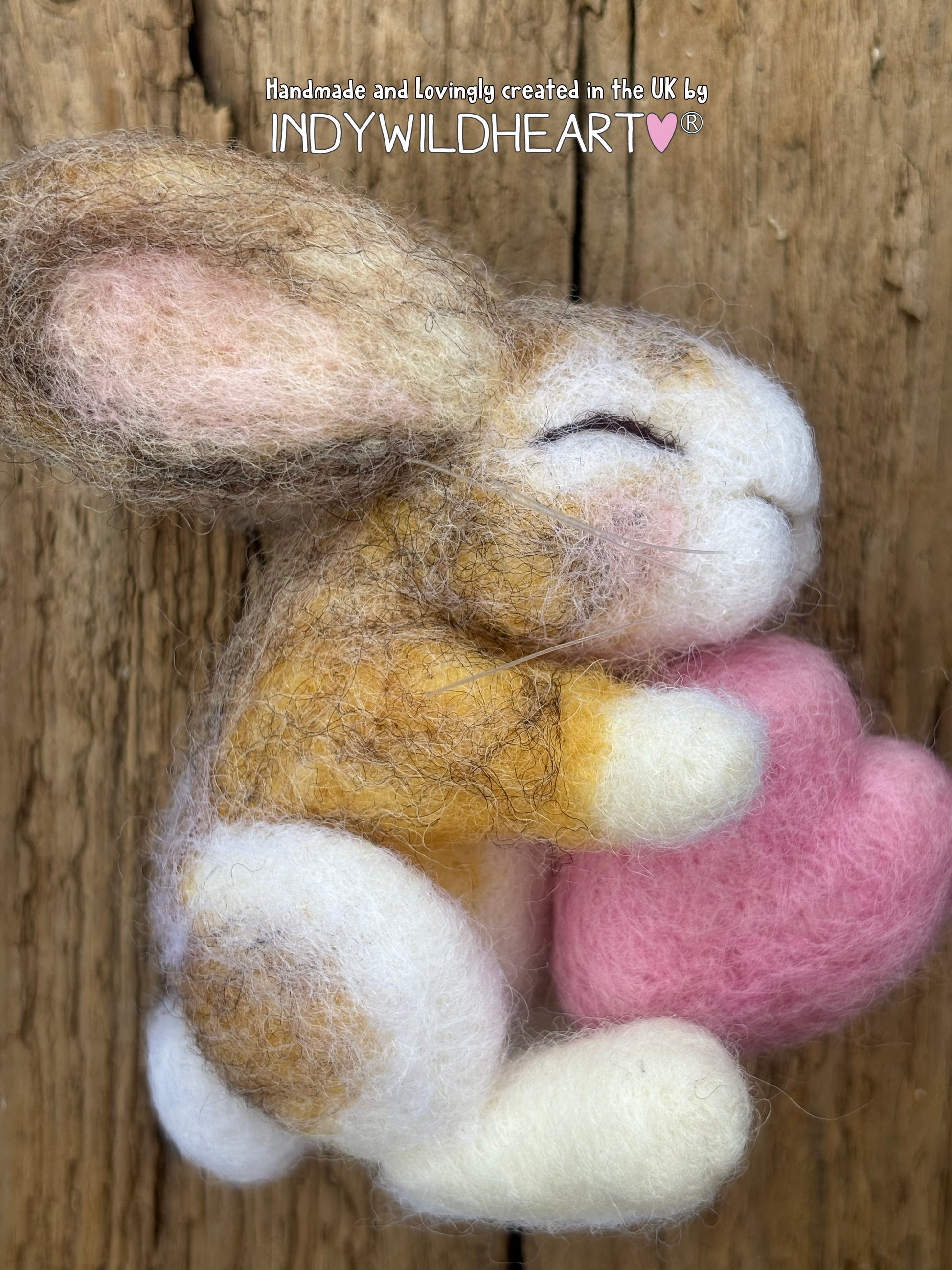 Needle Felted bunny asleep holding a pink heart on a wooden background