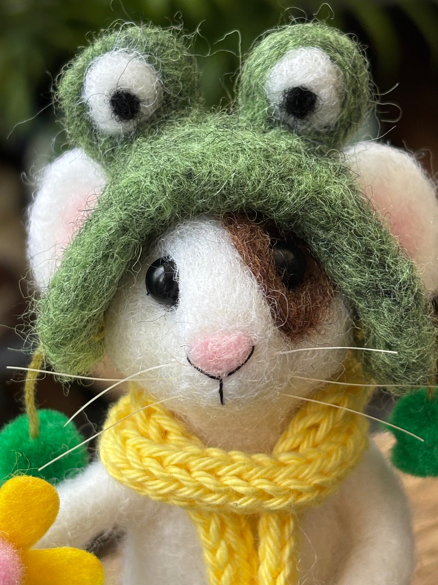 needle felted white mouse with brown patch over one eye, wearing a green frog hat.