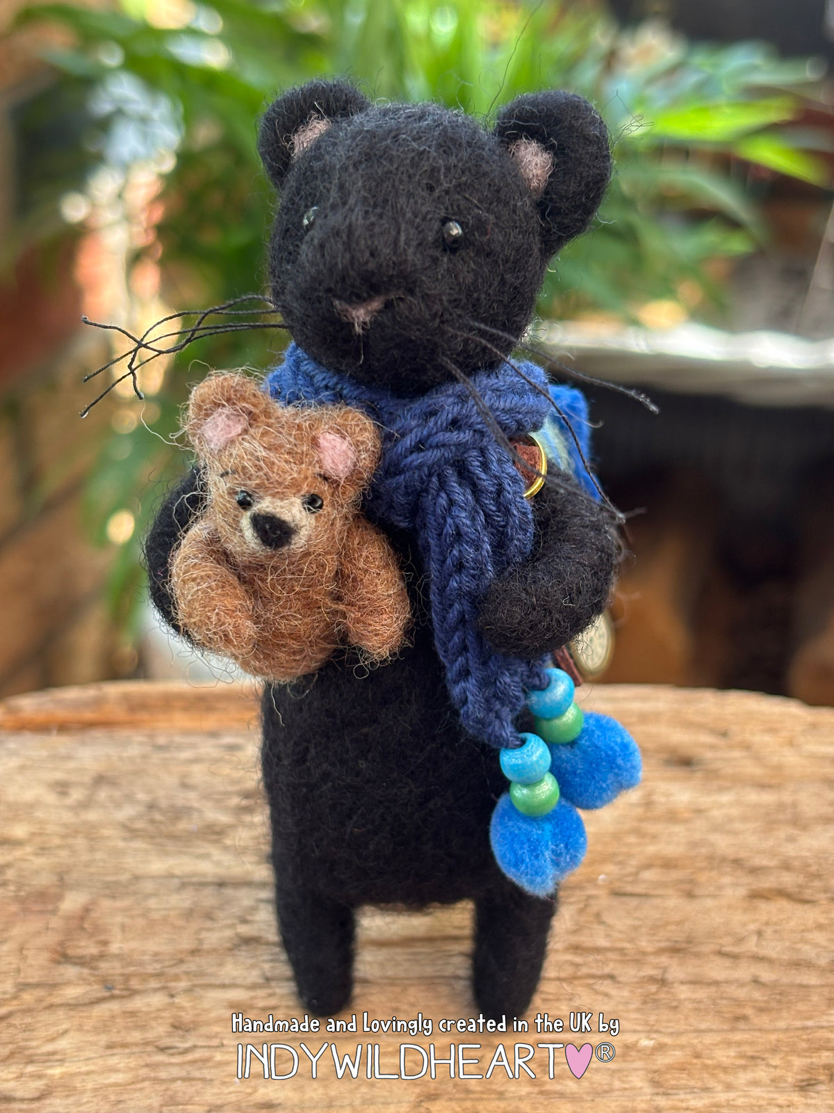 Needle Felted Black Panther character with navy blue scarf and holding a miniature needle felted teddy
