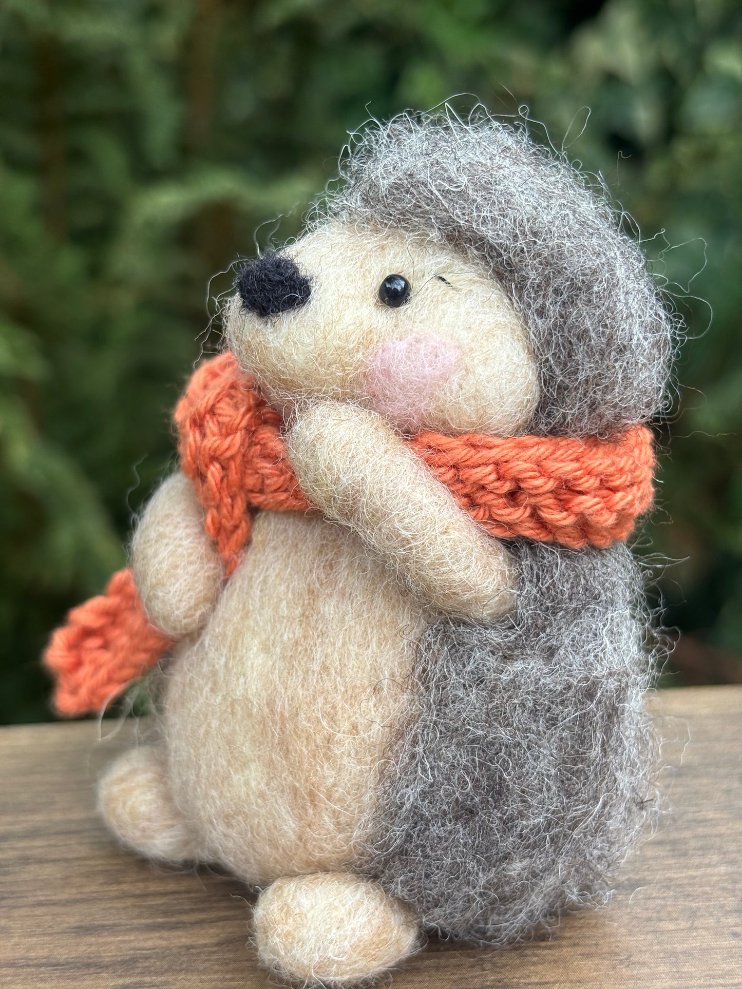 Hedgehog felt decoration with an orange scarf against a blurred green background