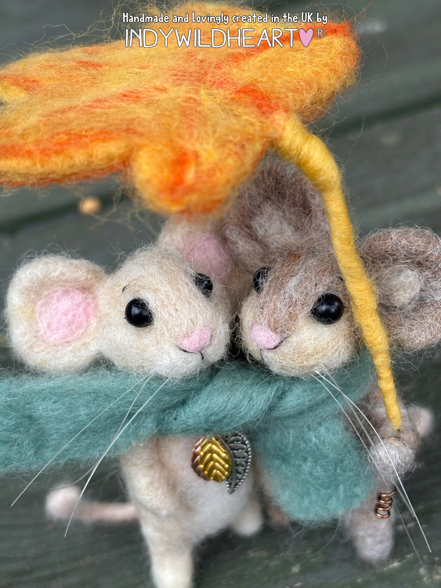 Handmade felted wool art piece featuring two small mice under a large orange leaf and yellow stem, wrapped in a teal scarf, on a dark wooden surface. Text overlay at the top reads 'Handmade and locally created in the UK By INDYWILDEART'.